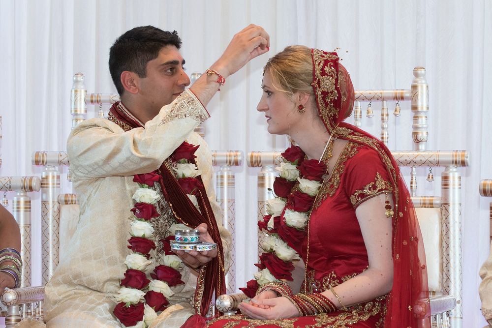 A couple in traditional wedding attire, the groom placing a wedding ornament on the bride's forehead.