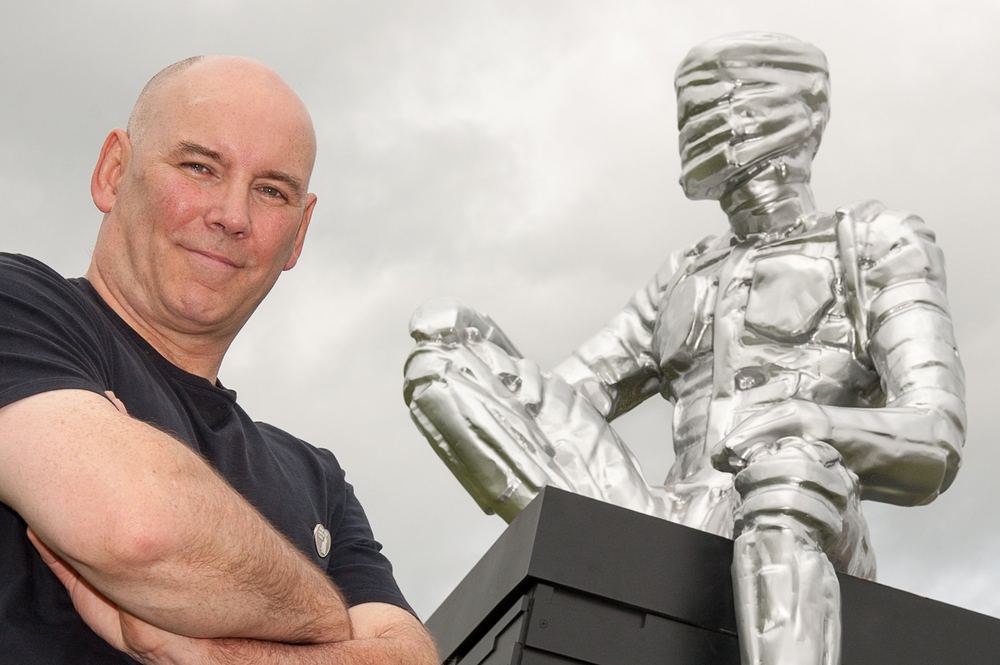 An artist stands with his sculpture, set high on a plinth.