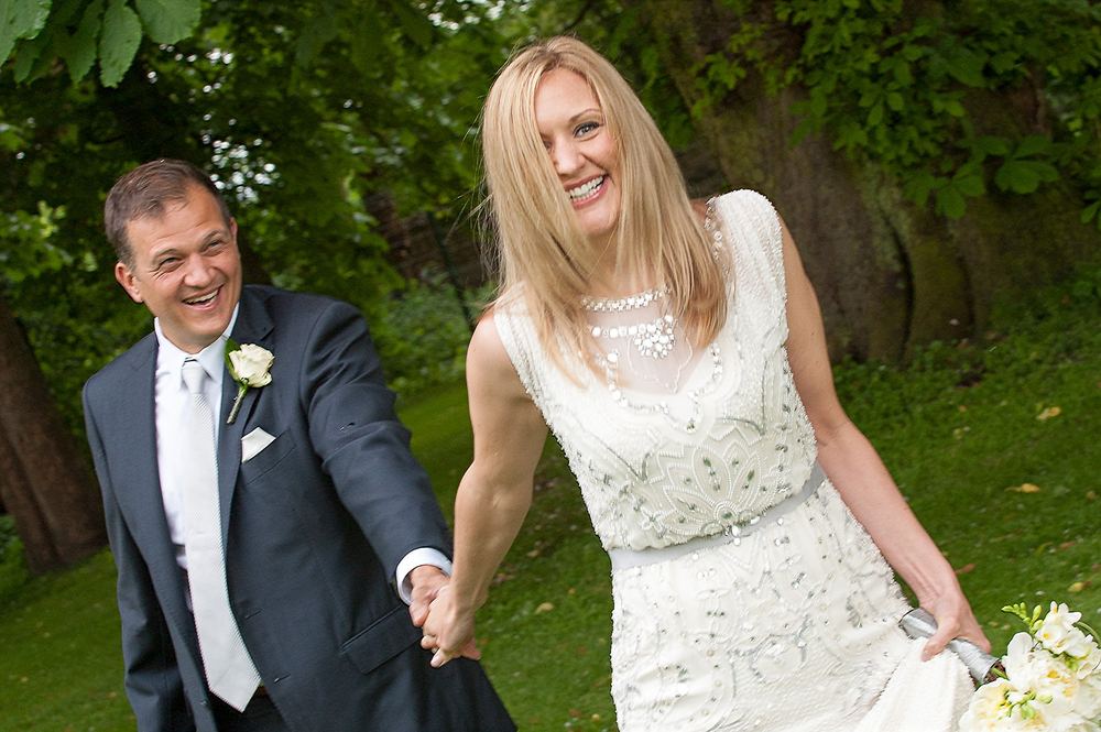 A smiling bride and groom hold hands in a garden setting.