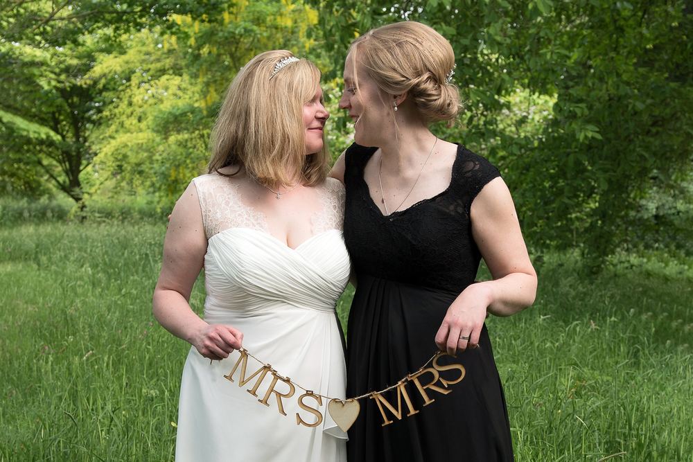 Helen & Hanneke hold a Mrs & Mrs sign after their wedding at The Little Theatre, Skipwith Hall, Escrick Park Estate.