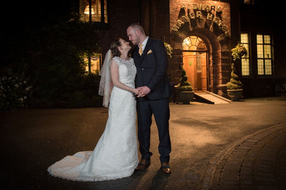 A night-time shot of Laura & Rob outside a floodlit Aldwark Manor, York.