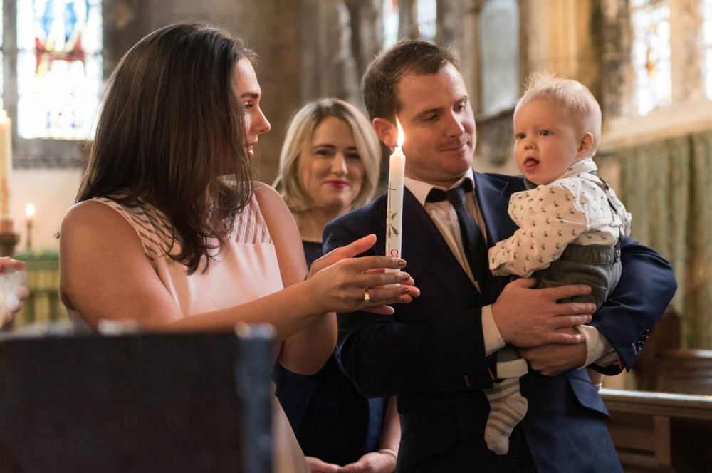 Parents hold a christening candle as the vicar blesses their baby.