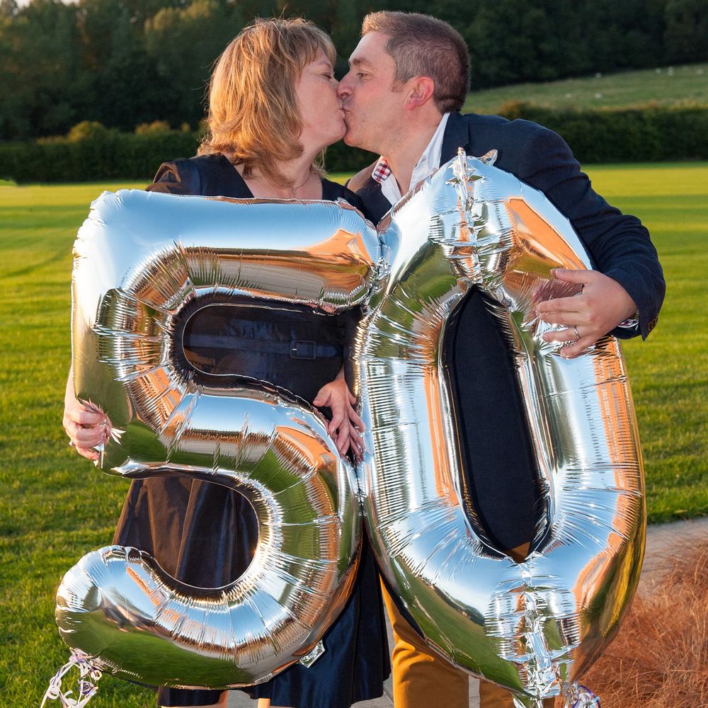 A couple kiss over a wall of 50 balloons.