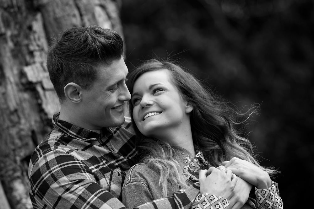An intimate black-and-white portrait of a joyful couple embracing outdoors.