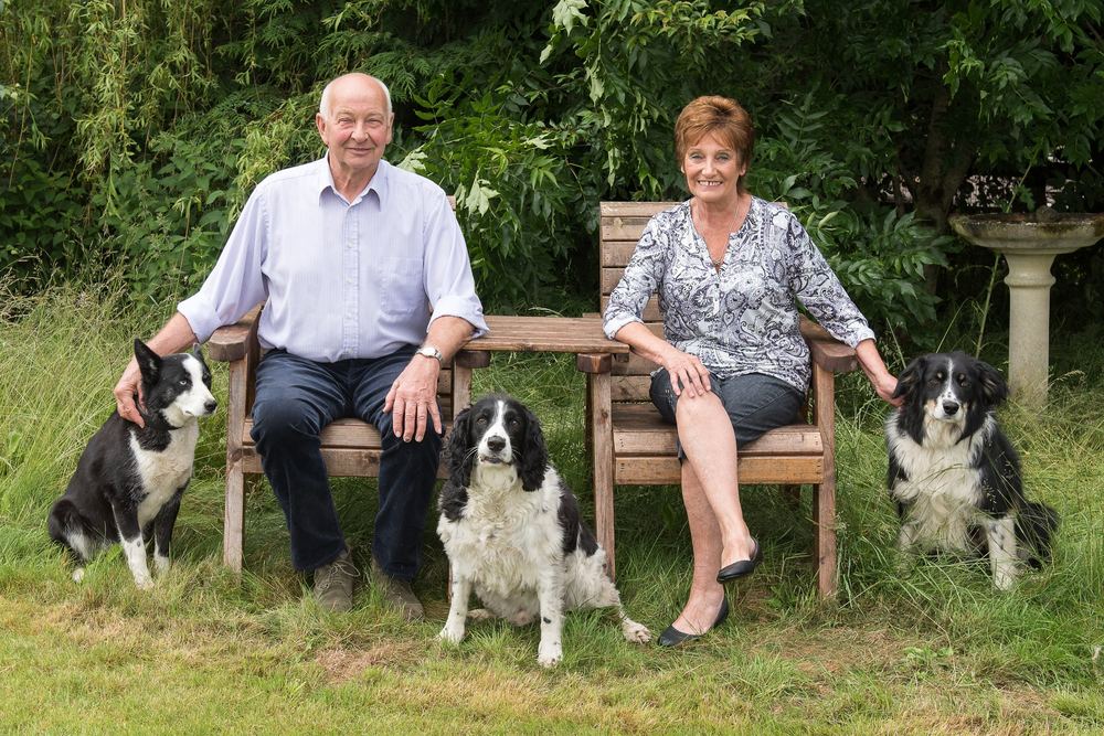 A couple sitting in their garden with their three dogs.