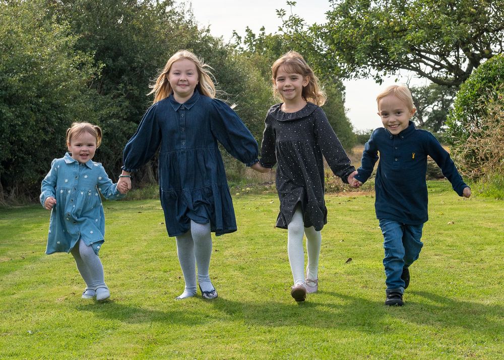 Four children holding hands, running toward the camera.