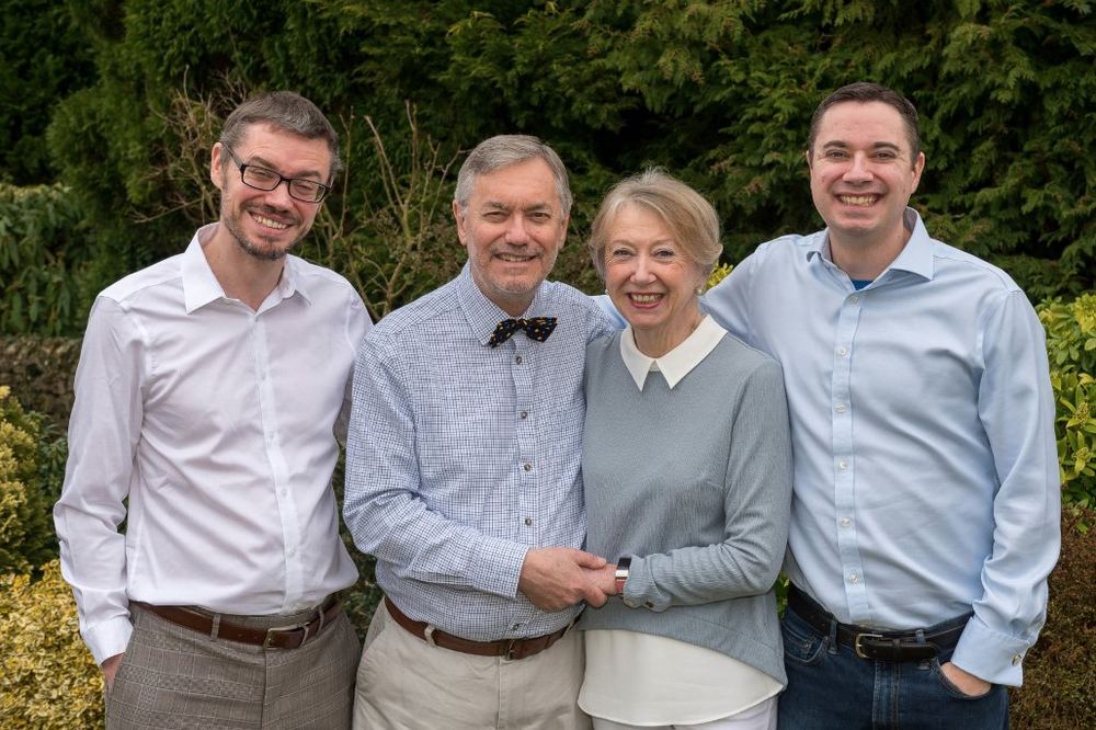 Parents and their two adult sons, dressed in pale colours, in the garden.