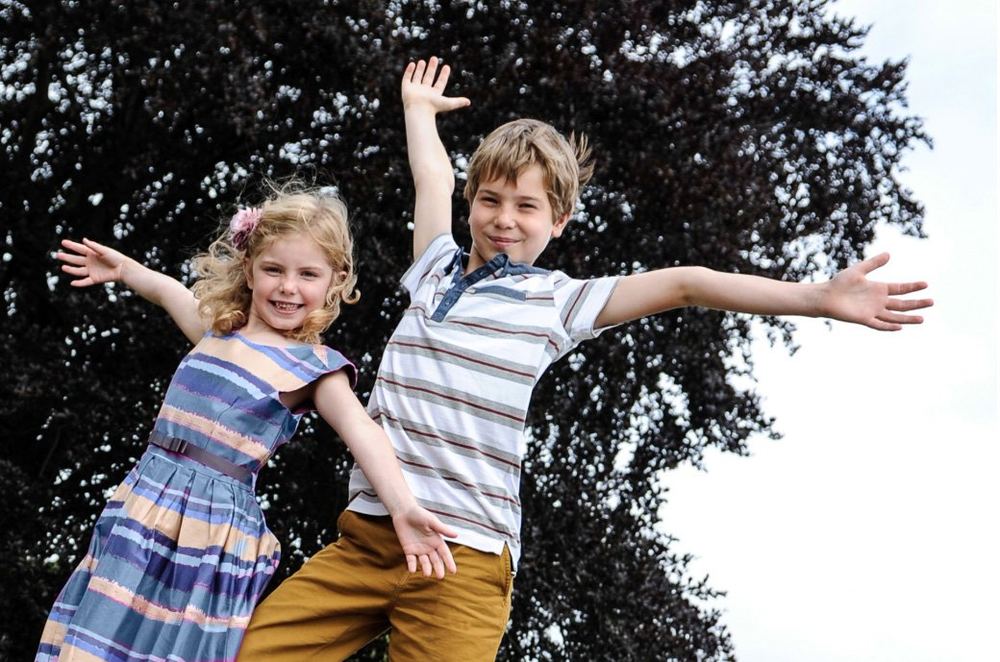 A brother and sister share a happy moment in the woods.