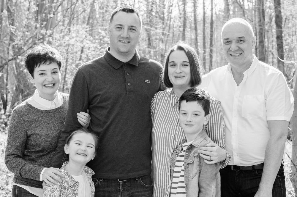 A black-and-white family portrait, four generations, in the woods.