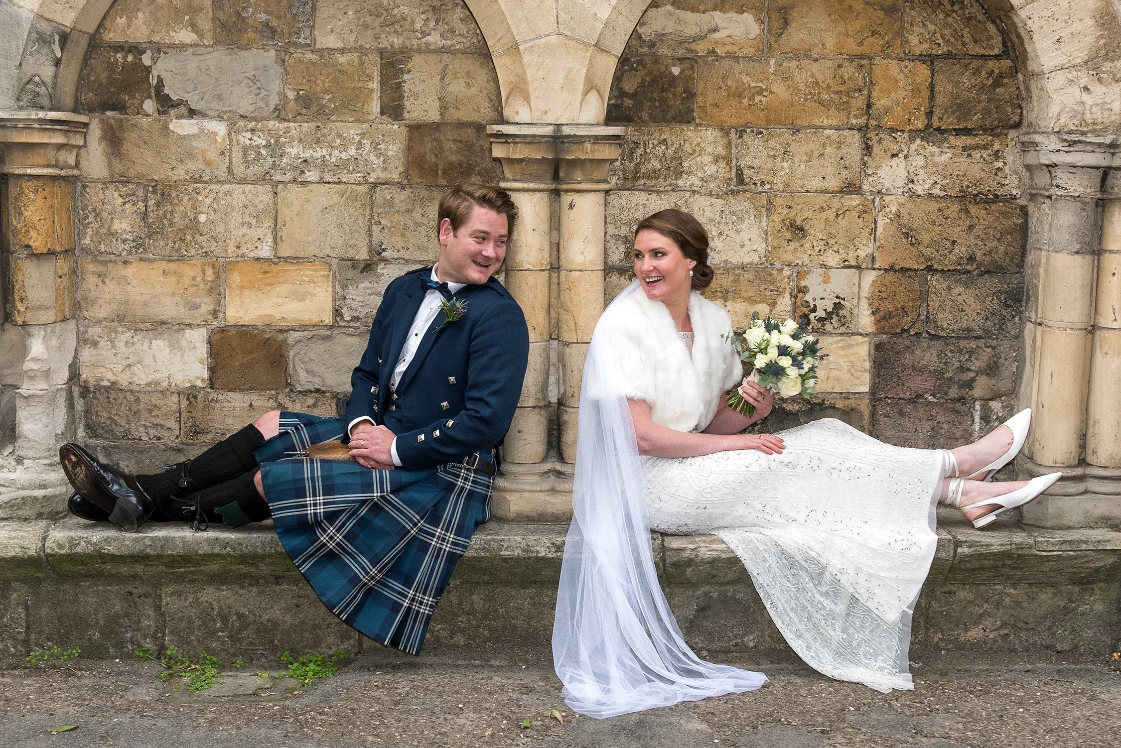 Bride and groom sitting on a stone bench beneath historic arches